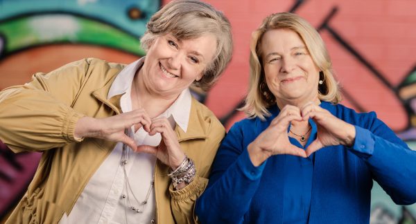 Two females holding up their hands in a heart shape.